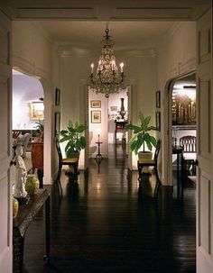 an open door leading to a hallway with chandelier and potted plants on either side