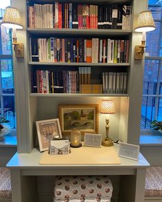 a white desk topped with a lamp next to a bookshelf filled with lots of books