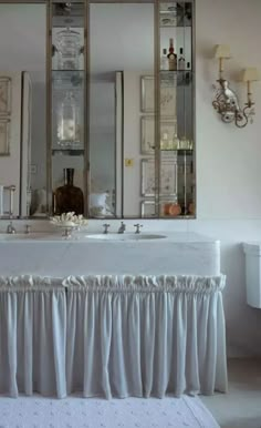 a white bathroom with two sinks and mirrors above it's counter top that has ruffles on the bottom