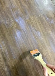 a person holding a paint brush on top of a wooden floor