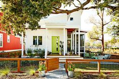 a small white house with red siding and green door in the front yard, surrounded by trees