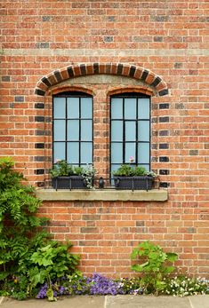 a brick building with two windows and plants