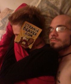 a man and woman laying in bed with a book on their head that reads strange beaver com