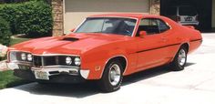 an orange muscle car parked in front of a garage