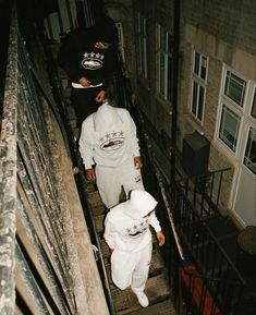 two people in white outfits walking up some stairs with their hands on the railings