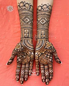 two hands decorated with henna designs on top of a red cloth covered tablecloth