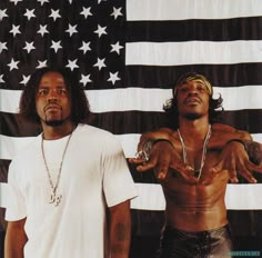 two men standing next to each other in front of an american flag with one pointing at the camera