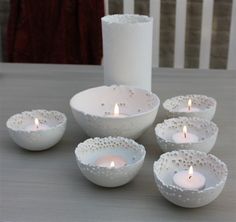 several white bowls with lit candles in them on a table next to a candle holder