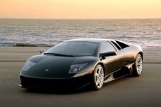 a black sports car parked in front of the ocean