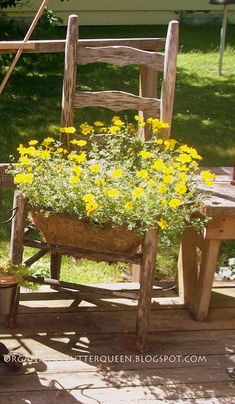 a wooden chair sitting on top of a porch next to a planter filled with yellow flowers