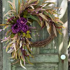 a wreath with purple flowers and green leaves on a wooden door, next to a candle