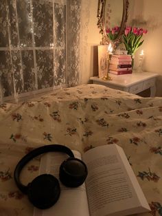 an open book and headphones on a bed with floral bedspread in front of a window