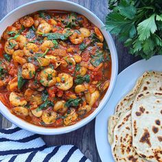 a bowl of shrimp stew next to some pita bread and parsley on the side