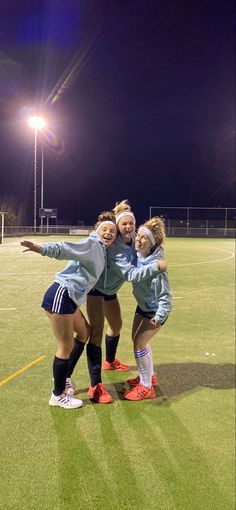 three girls on a soccer field with their arms around each other