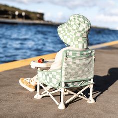 a lawn chair with a hat on it is sitting next to the water and has a strawberry in its lap