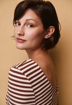 a woman with short hair wearing a brown and white striped top looking off to the side