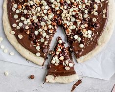 a chocolate pizza with nuts on top and one slice cut out from the other side