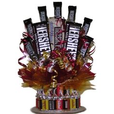 an arrangement of chocolates and candy bars in a glass vase with ribbons on it