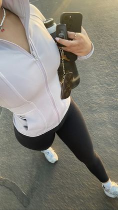 a woman in white shirt and black leggings holding cell phone