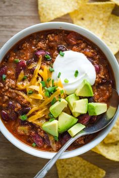 a white bowl filled with chili, cheese and avocado next to tortilla chips