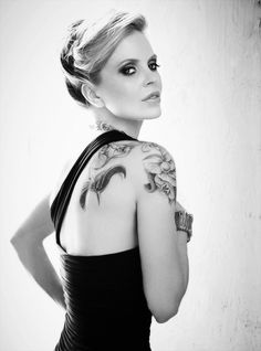 a woman in a black dress with tattoos on her back and shoulder is posing for the camera