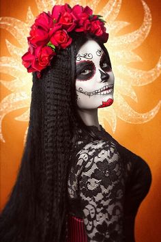 a woman with long black hair and red flowers in her hair wearing a skeleton make up