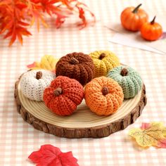 small crocheted pumpkins sitting on top of a wooden plate next to fall leaves