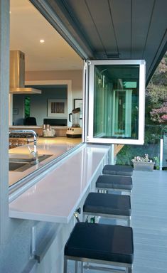 an outdoor kitchen with bar stools next to the counter top and windows on the outside wall