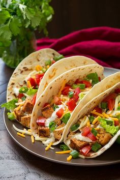 three tacos on a plate with limes and tomatoes