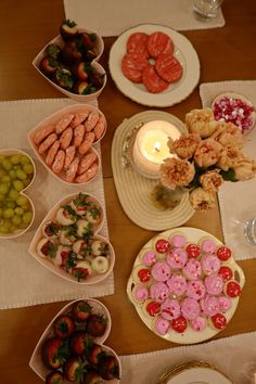 a table topped with lots of plates and bowls filled with different types of food next to a candle