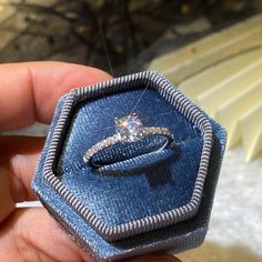 a person holding a ring in a blue box with diamonds on it's side