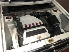 the engine compartment of a white car with its hood open and it's lights on