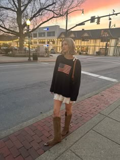 a woman is standing on the sidewalk in front of a street light and building with an american flag t - shirt