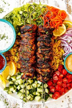 a platter filled with grilled meat, vegetables and dips on skewers