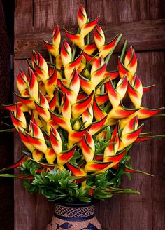 a vase filled with yellow and red flowers on top of a wooden table next to a wall