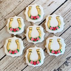 six decorated cookies with gold horseshoes and pink roses on them sitting on a wooden table