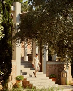 a man walking up some steps in front of a house with trees and bushes on either side