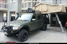 an suv parked in front of a building with a roof tent on it's top