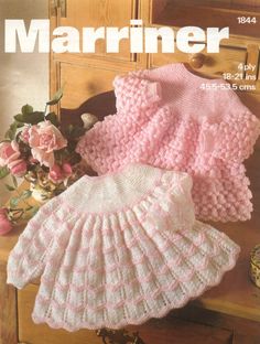 two knitted baby sweaters and a crochet dress on a wooden table