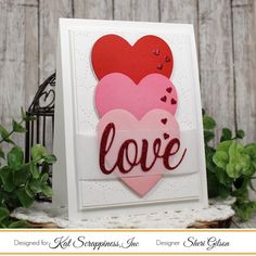 a card with two hearts and the word love written in red on it, next to some green leaves