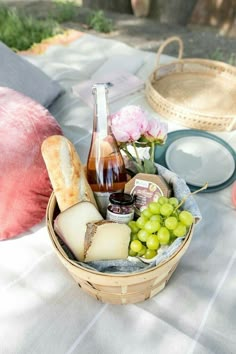 a picnic basket with wine, cheese and bread on a blanket outside in the sun