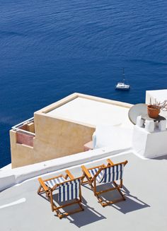 two wooden chairs sitting on top of a roof next to the ocean with a boat in the distance