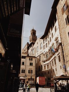 some people are walking down the street in an old town with stone buildings and tall towers