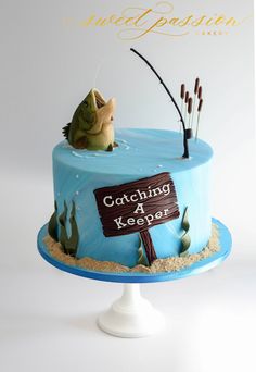 a blue cake with a fishing theme on the side and a sign that says catching a keeper