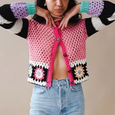 a woman with her hands on her hips wearing a pink and black crochet sweater