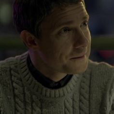 a man wearing a gray sweater and black collared shirt looking at something in the distance