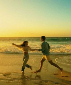 a man and woman running on the beach at sunset with waves crashing in front of them