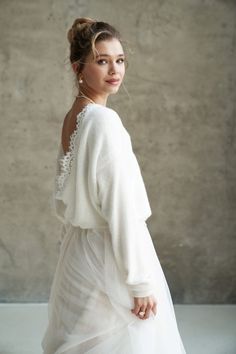 a woman in a white dress is standing near a wall and looking at the camera