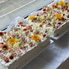 two rectangular cakes with flowers on them sitting on a table in front of a window