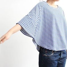 a woman standing in front of a white wall wearing a blue and white striped top